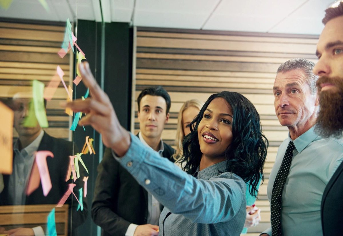 A woman pointing to the wall with sticky notes on it.